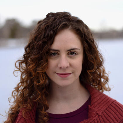 Headshot of woman with long, brown curly hair with bold, friendly expression.